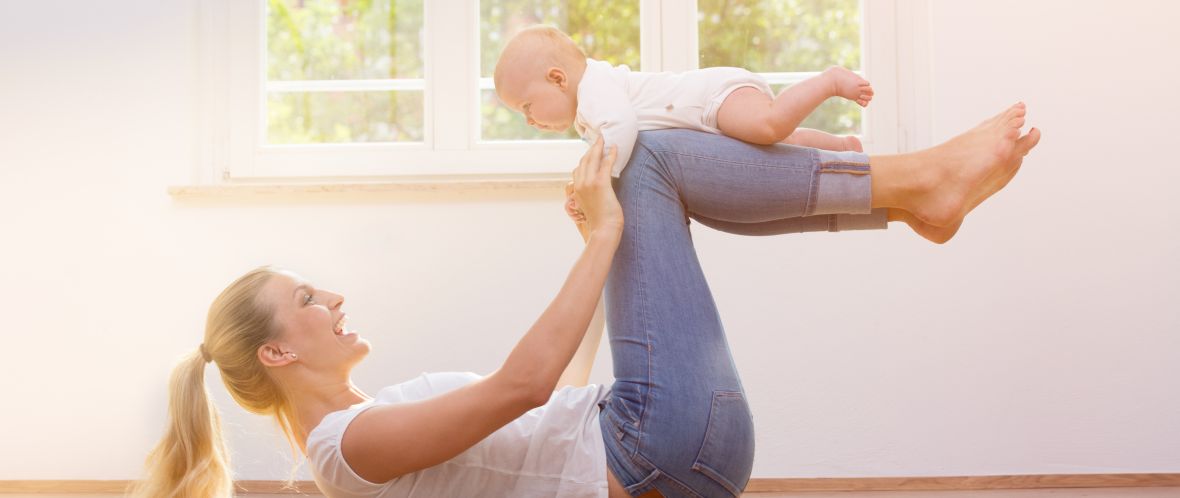Frau liegt auf ihrem Rücken und trägt ihr Baby auf ihren angezogenen Beinen