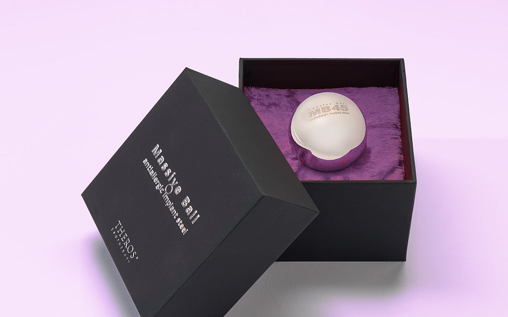 Theros® Massive Balls: Sehr schwere Kugeln aus massivem, antiallergenem Edelstahl (Implantatstahl) für Frauen und Männer zum Beckenbodentraining in waagerechten Positionen oder zur Prostatastimulation in einer schwarzen Schachtel mit erhabenem Logo und Kissen aus dunkel-violettem Samt.