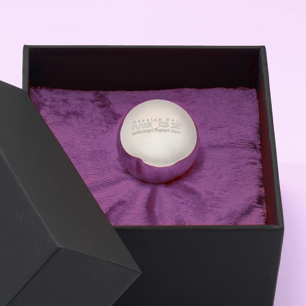 Theros® Massive Ball MB32 – esfera maciza de 32 mm de acero inoxidable antialérgico para mujeres y hombres para el entrenamiento del suelo pélvico en posiciones horizontales o para la estimulación de la próstata en una caja negra sobre terciopelo violeta oscuro, vista detallada.